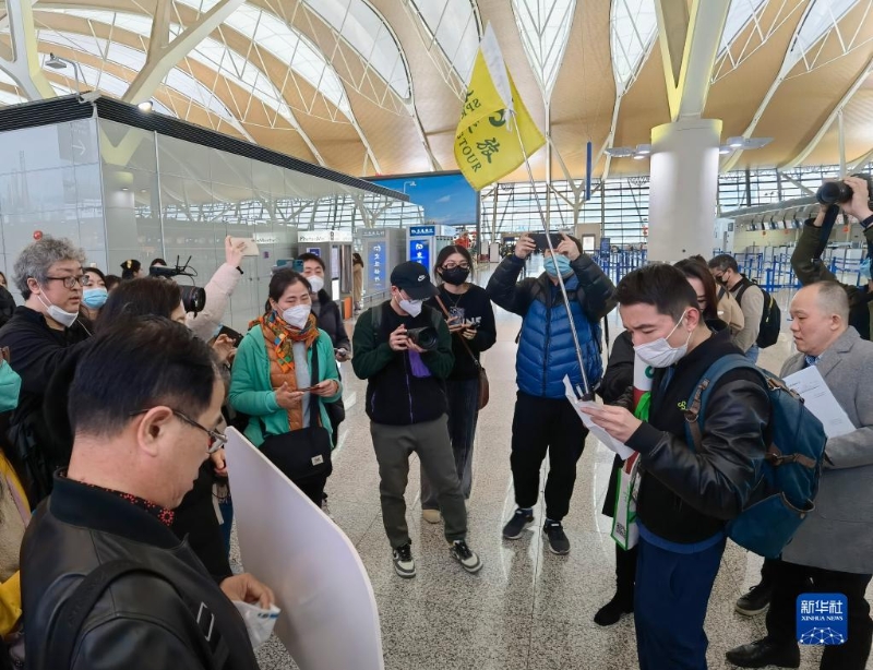 2月6日，在上海浦東國際機場，出境團隊游領隊師文（舉旗者）向游客說明相關注意事項。（圖源：新華社）